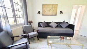 Un salon comprenant un canapé, deux fauteuils, une table basse en verre et un tableau accroché au mur.