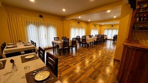 Comedor con varias mesas y sillas, suelo de madera y cortinas amarillas.