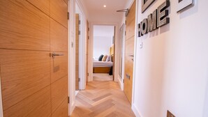 Un couloir avec des portes en bois, un lit à l’arrière-plan et un panneau indiquant « MAISON » sur le mur.