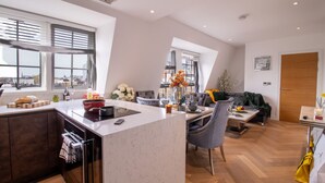 Une cuisine moderne dotée d’un îlot central, d’un coin repas avec un canapé et de grandes fenêtres offrant une vue sur la ville.