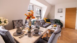 Un coin repas avec une table dressée pour deux personnes, un canapé et une fenêtre avec des stores.
