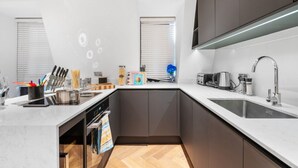 Ett modernt kök med en central köksö, inbyggda vitvaror och en stor diskho.