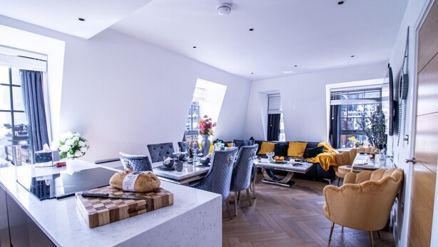 A modern kitchen with a marble countertop, a dining area with blue chairs, and a sofa with yellow cushions. - Marble Arch Penthouse 73, Best Location! (Greater London)