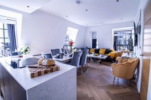 A modern kitchen with a marble countertop, a dining area with blue chairs, and a sofa with yellow cushions.