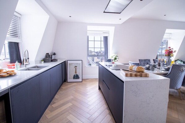 A modern kitchen with dark cabinetry, a marble island, and a view of the city through large windows.