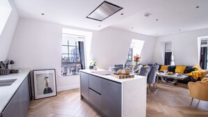 A modern kitchen with a central island, large windows, and a dining area with a sofa and table. - Marble Arch Penthouse 73, Best Location! (Greater London)