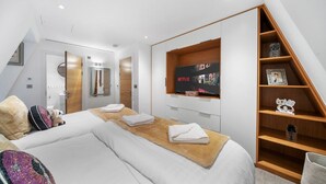 A modern hotel room with two beds, a wooden shelf unit, a TV mounted on the wall, and a bathroom visible through an open door. - Marble Arch Penthouse 73, Best Location! (Greater London)