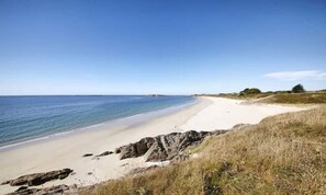 Une plage avec un ciel dégagé, un rivage sablonneux et des affleurements rocheux.