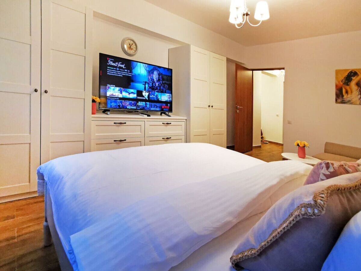 Quarto com uma cama grande, televisão sobre uma cômoda e porta que dá para outro espaço.