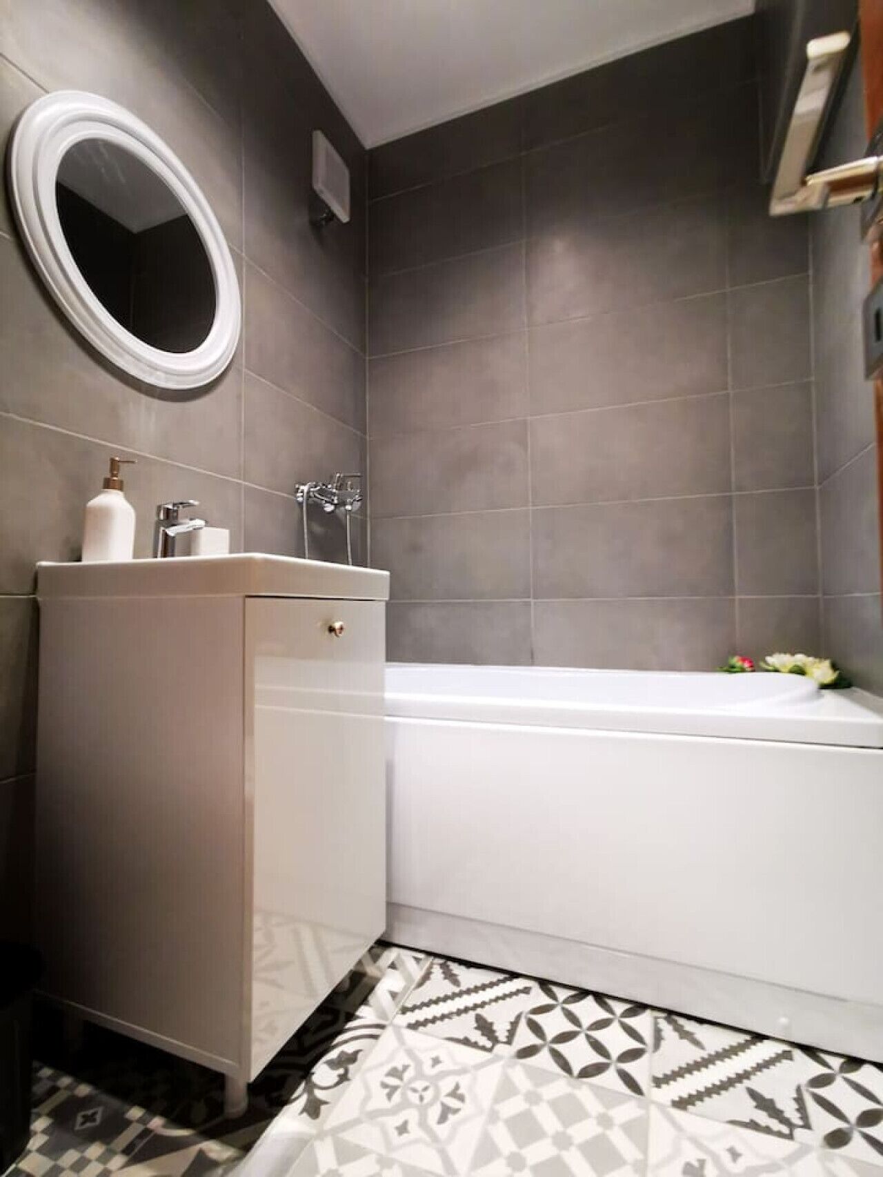 A bathroom with a bathtub, a vanity with a mirror, and a patterned floor.