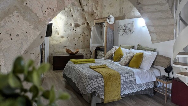 Ein gemütliches Schlafzimmer mit rustikalem Stein-Gewölbe, einem Bett mit gemusterten Betttextilien und einem kleinen Nachttisch.