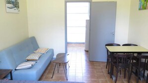 Una habitación con un sofá azul, una mesita, una mesa de comedor con sillas y una puerta que da al exterior.