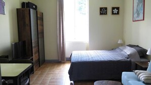Un dormitorio con cama, escritorio, silla, sofá y ventana con cortinas.