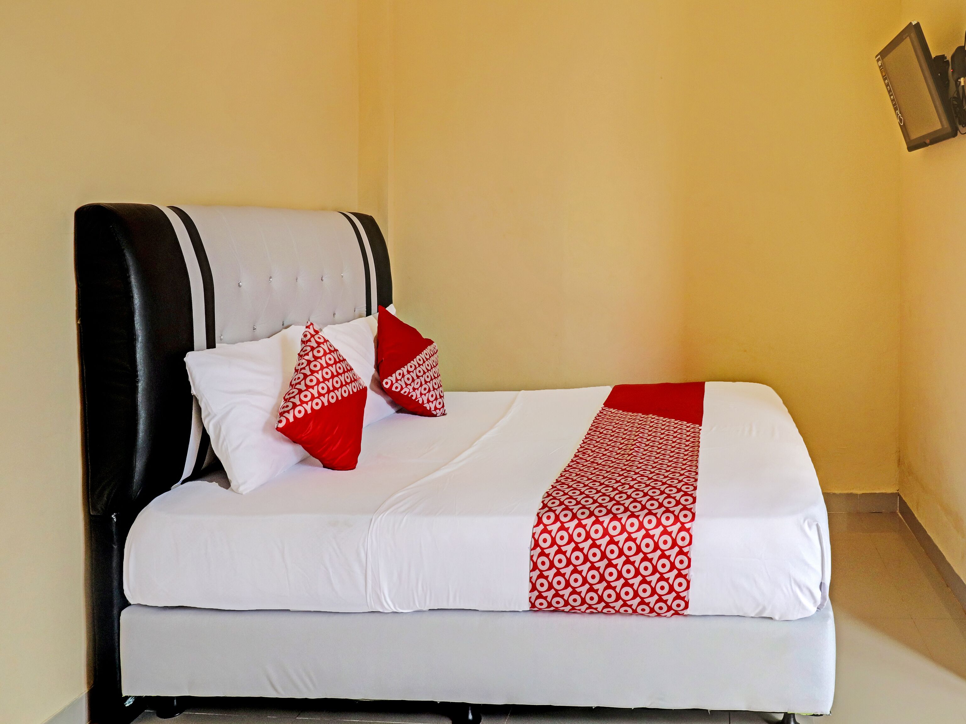A neatly made bed with white bedding and red accents, a black headboard, and a yellow wall.
