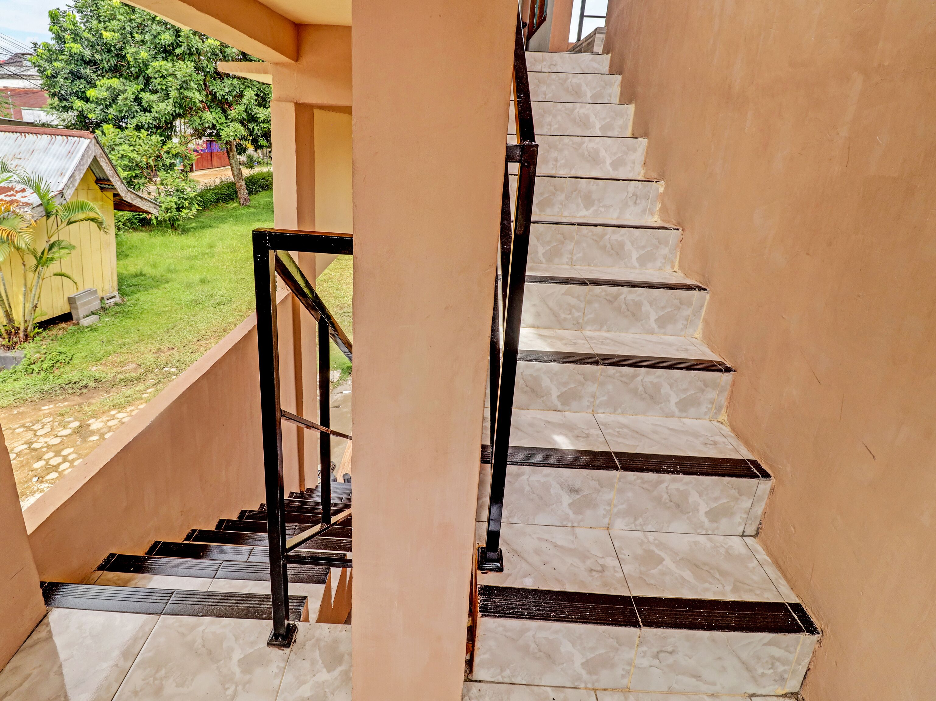 Eine Treppe mit weißen Marmorstufen und schwarzen Geländern, die zu einem überdachten Außenbereich mit Blick auf einen Garten und ein kleines Gebäude führt.