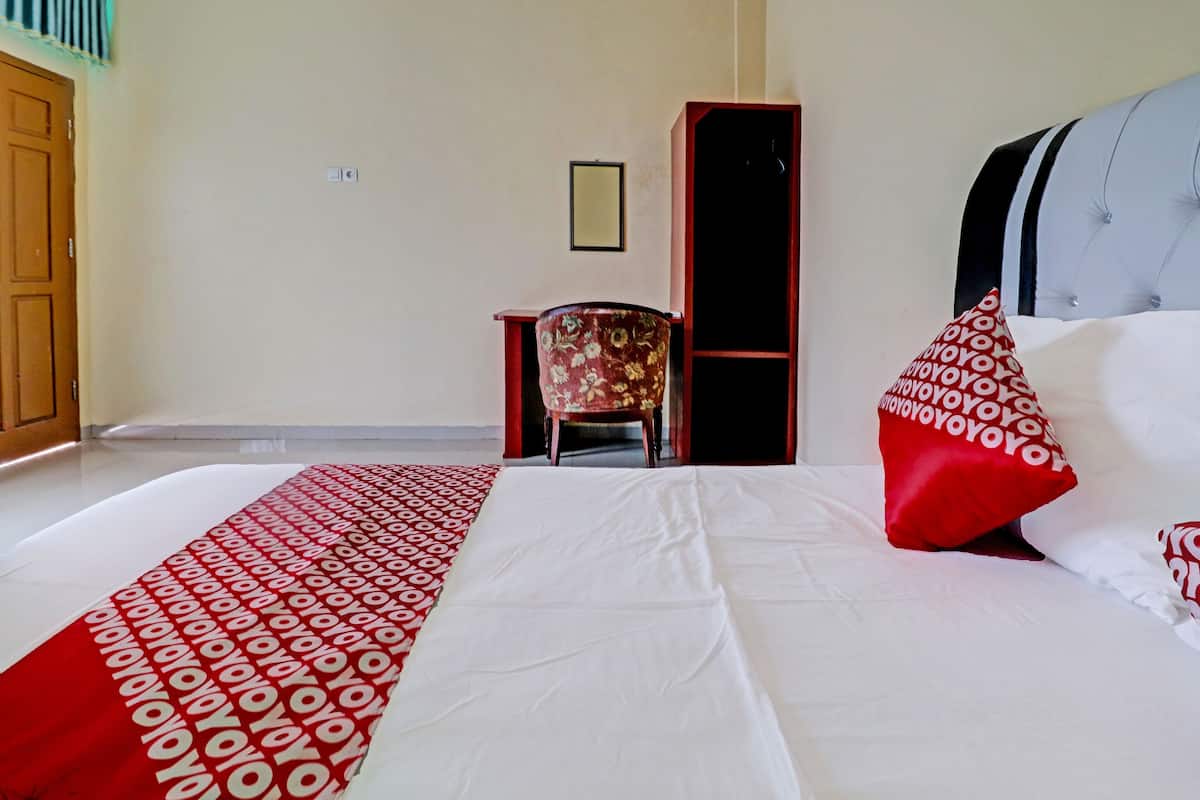 A hotel room with a neatly made bed, a chair, a wardrobe, and a door.