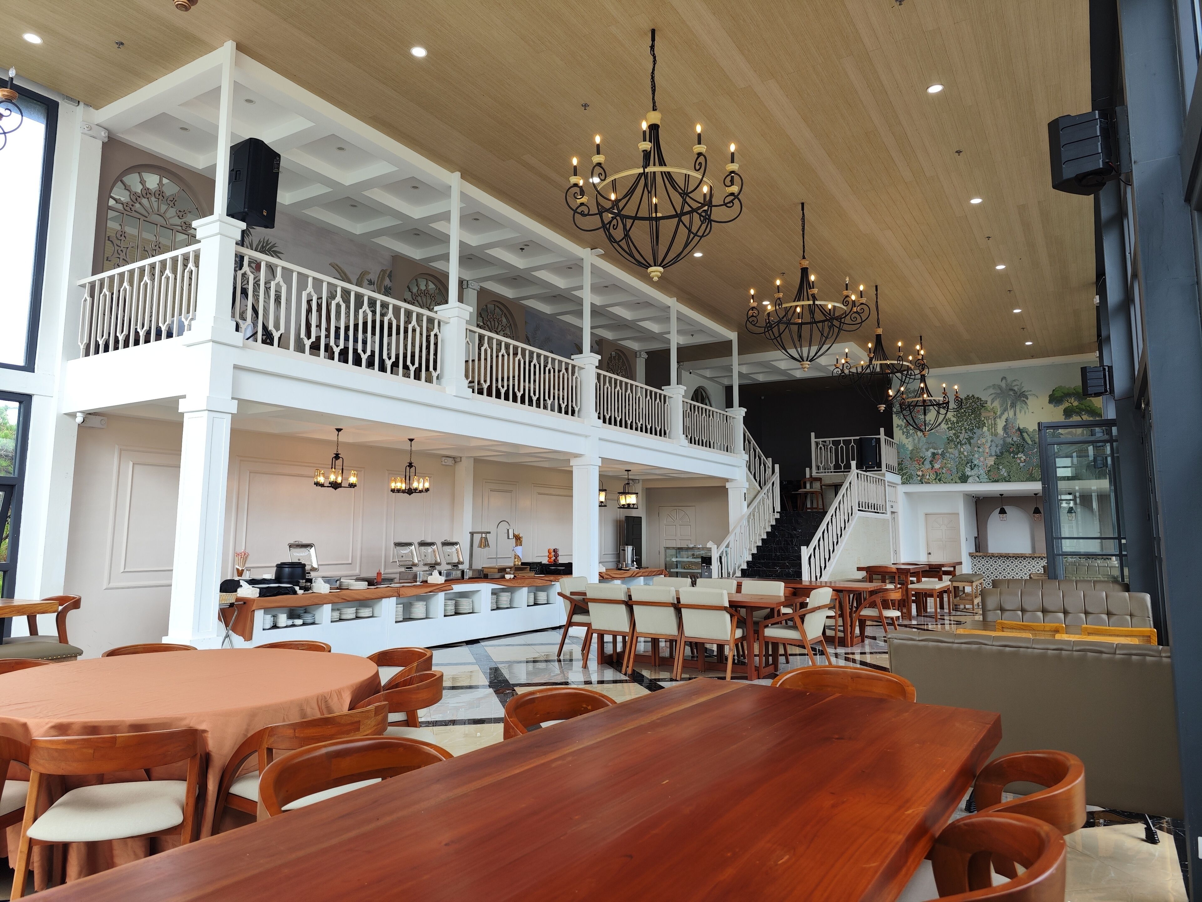A spacious restaurant with high ceilings, multiple dining areas, and a staircase leading to an upper level.