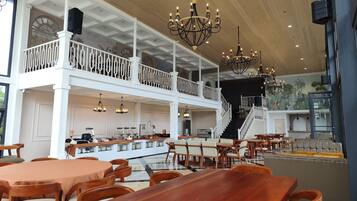 A spacious restaurant with high ceilings, multiple dining areas, and a staircase leading to an upper level.