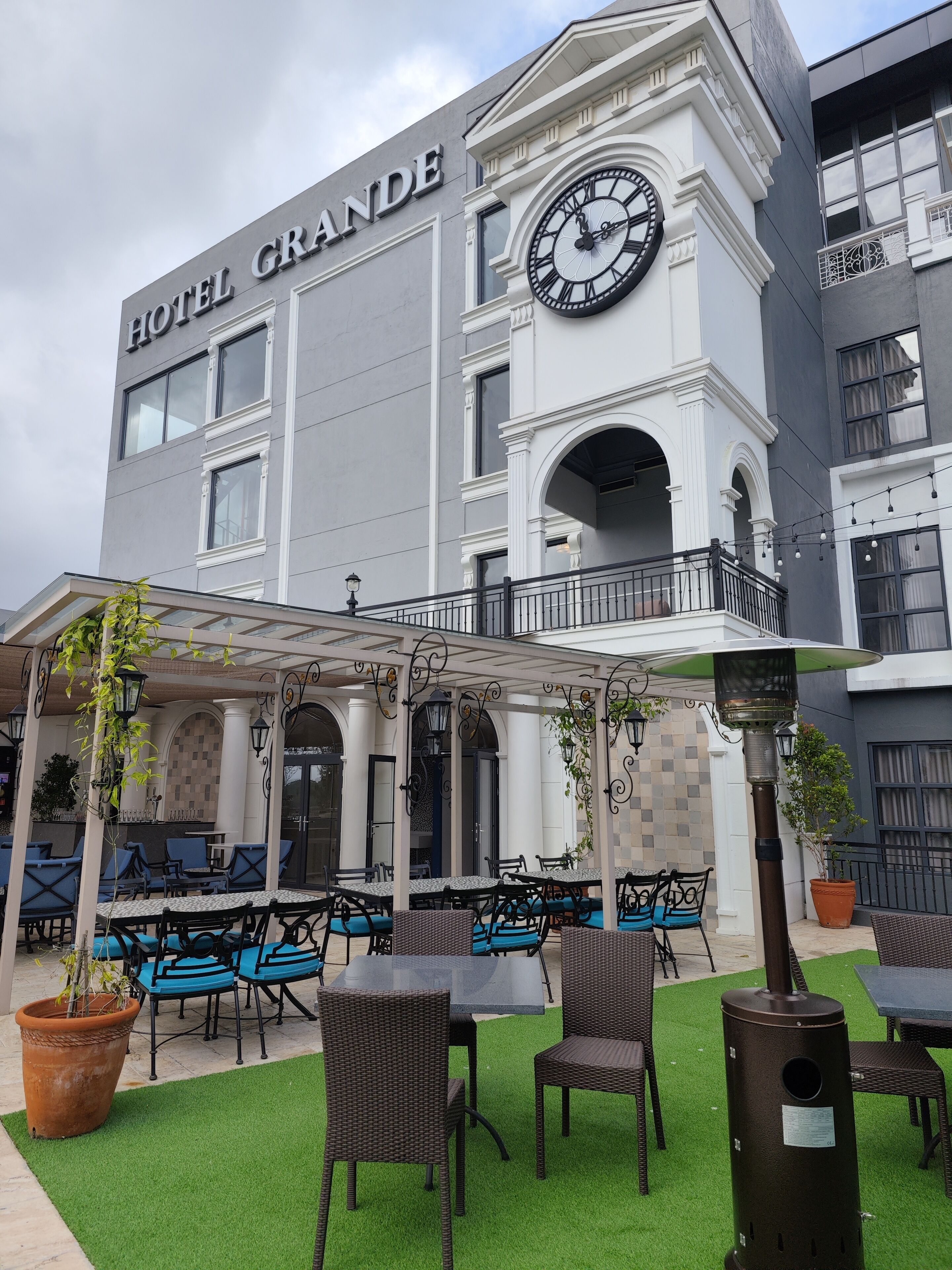 A hotel named "HOTEL GRANDE" with outdoor seating and a clock on the facade.