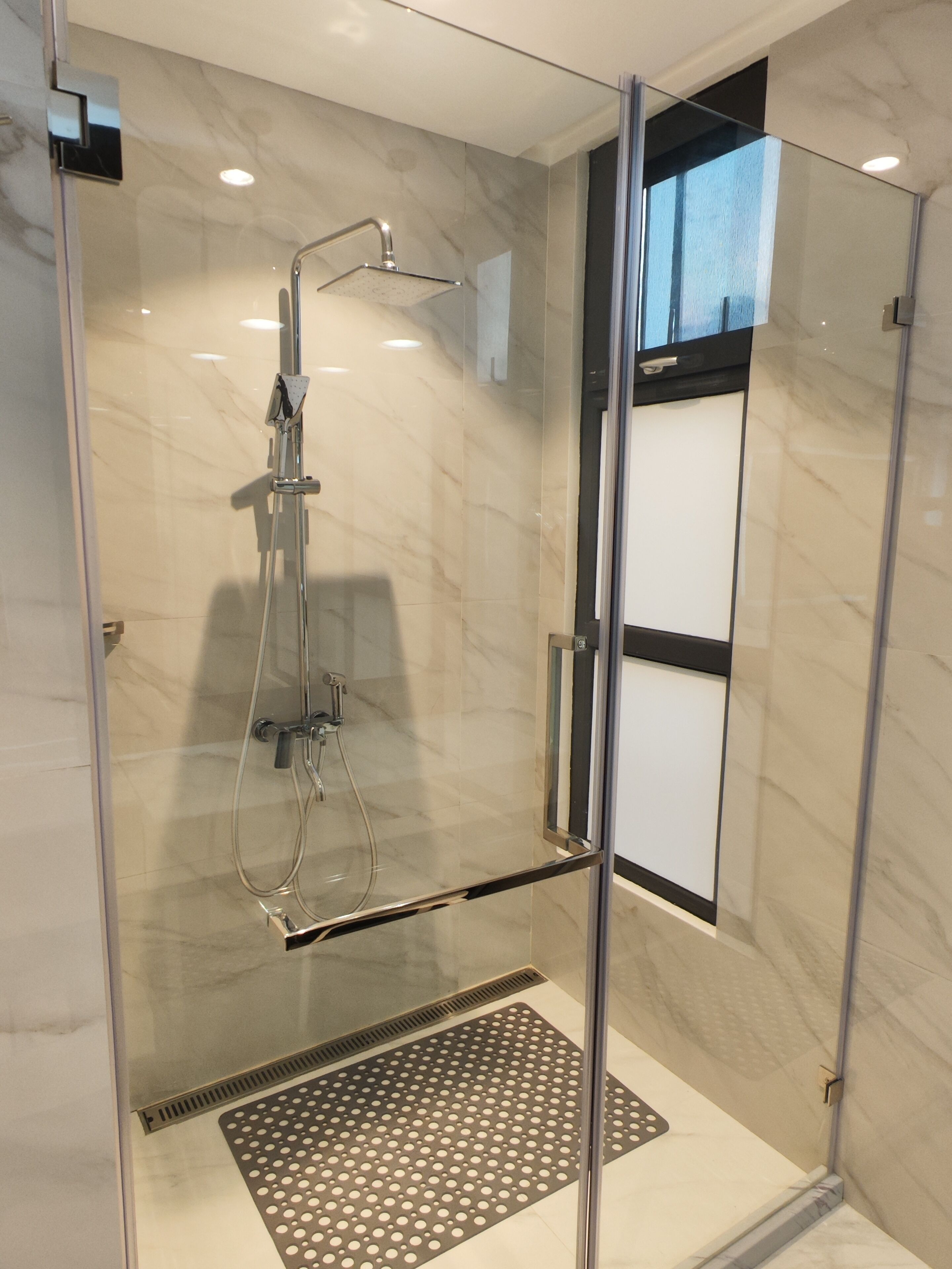 A modern shower with a glass door, a handheld showerhead, and a control panel.