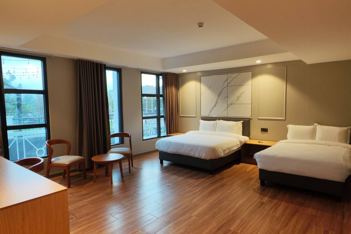 A hotel room with a large bed, a smaller bed, a desk, a chair, and a view of the outdoors.