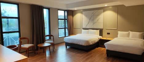 A hotel room with a large bed, a smaller bed, a desk, a chair, and a view of the outdoors.