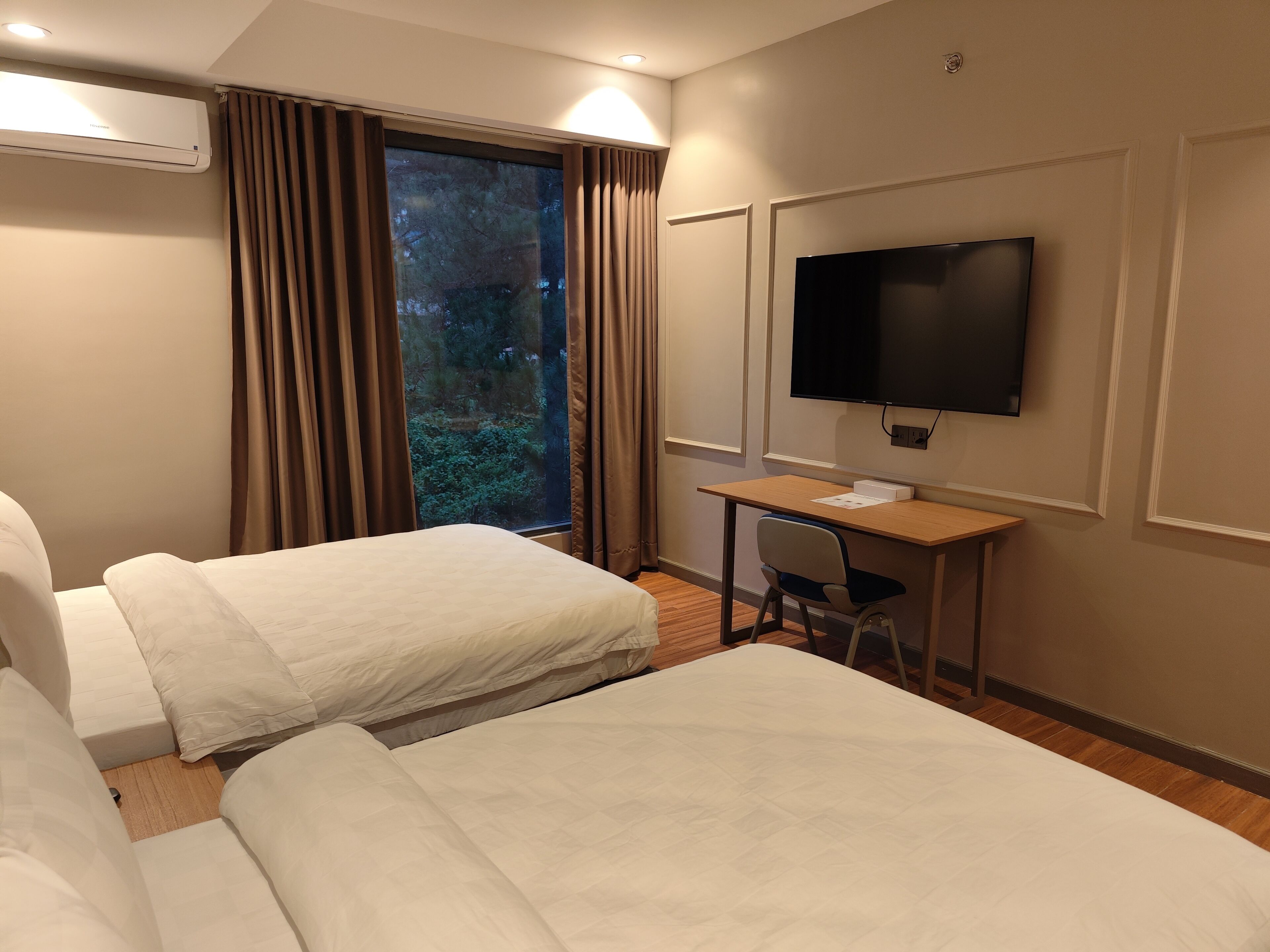 Une chambre d’hôtel avec deux lits, un bureau, une chaise, une télévision et une fenêtre avec des rideaux.