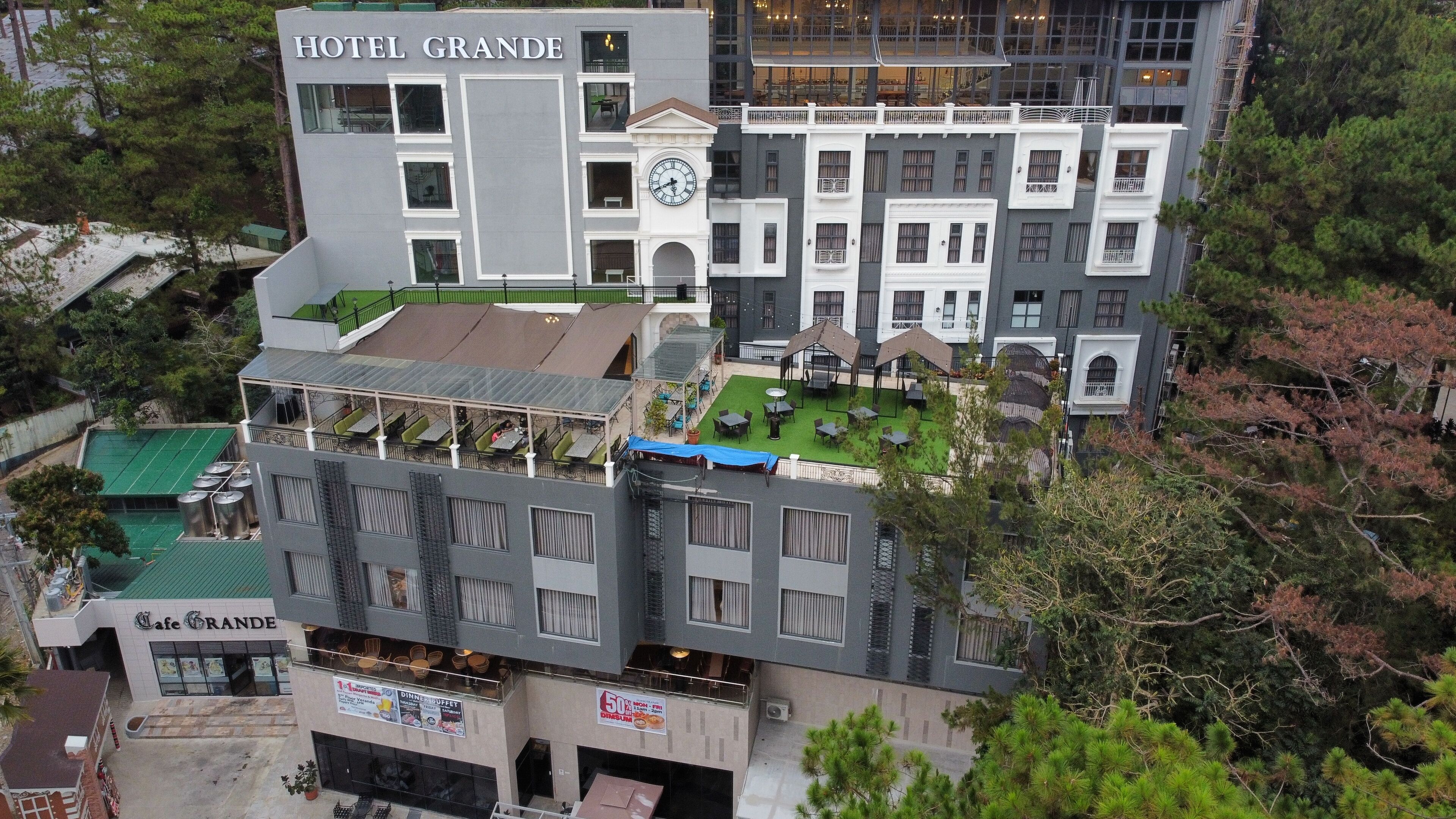 Un hotel de varios pisos con una terraza en la azotea, un comedor y una torre con un reloj visible.