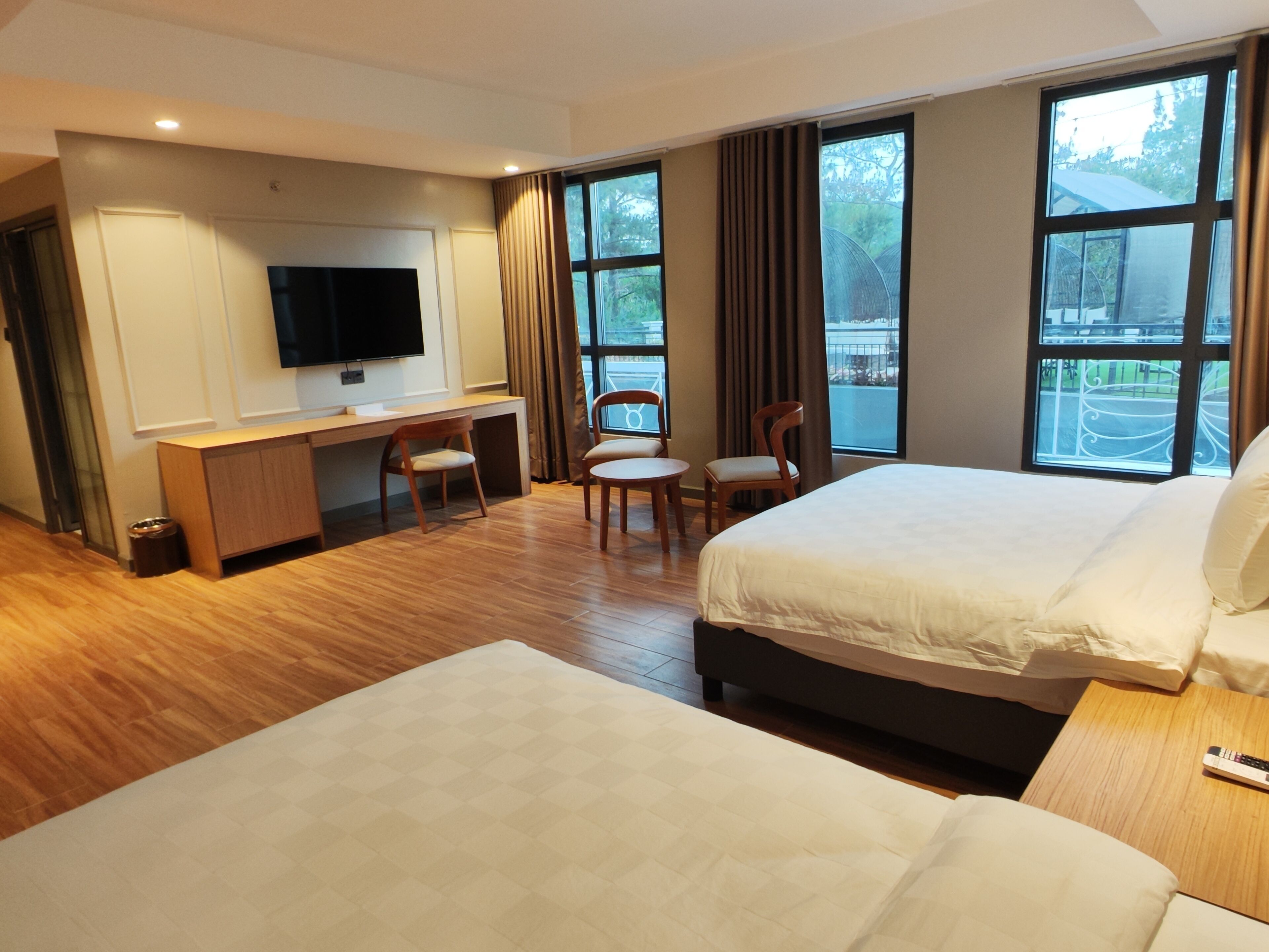 Hotelkamer met twee bedden, een bureau met stoel, een televisie en grote ramen.