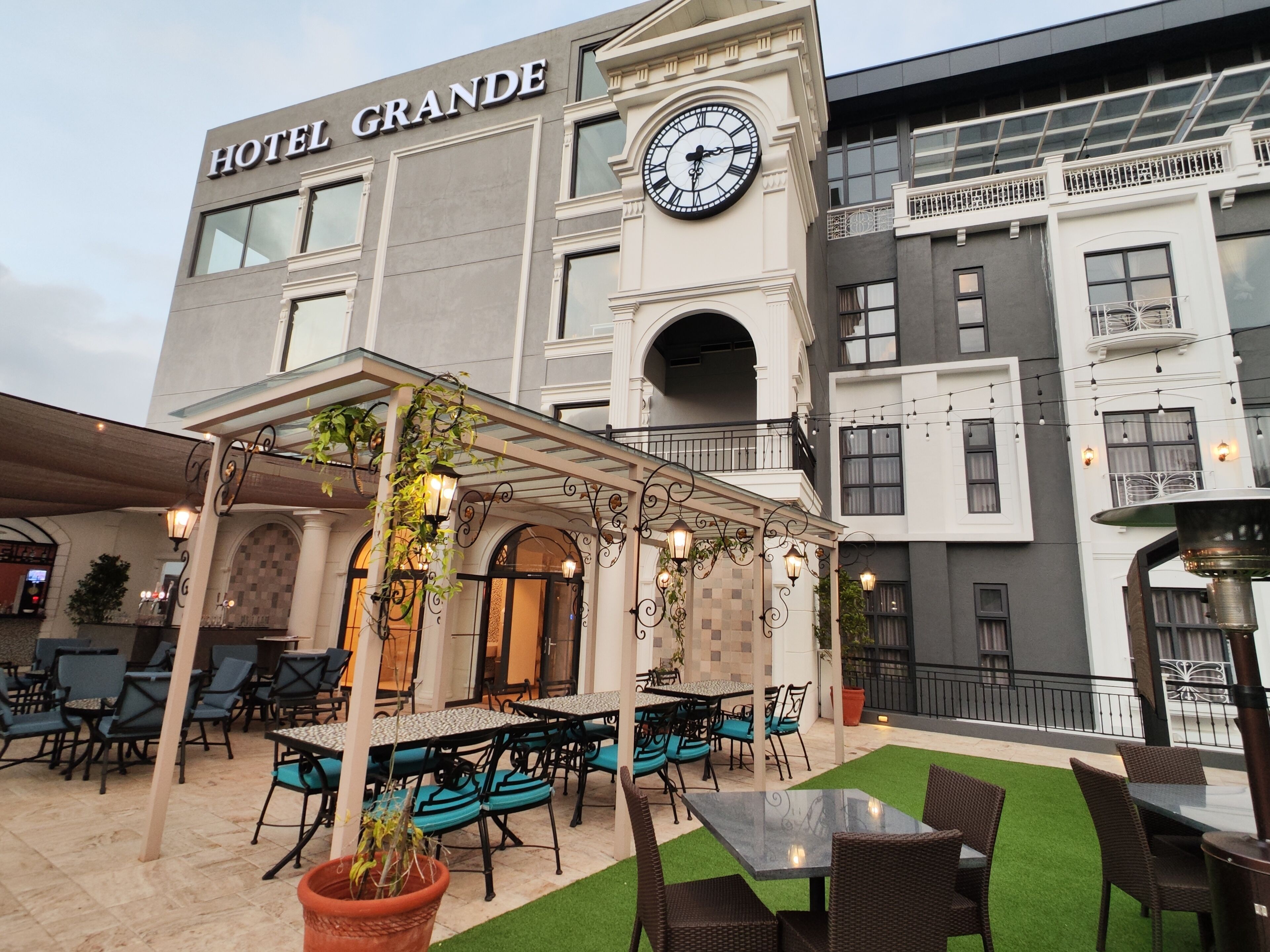 A hotel with outdoor seating, a clock, and a sign reading "HOTEL GRANDE".