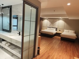 A modern hotel room with a large mirror, two beds, a wooden floor, and a marble-tiled vanity.
