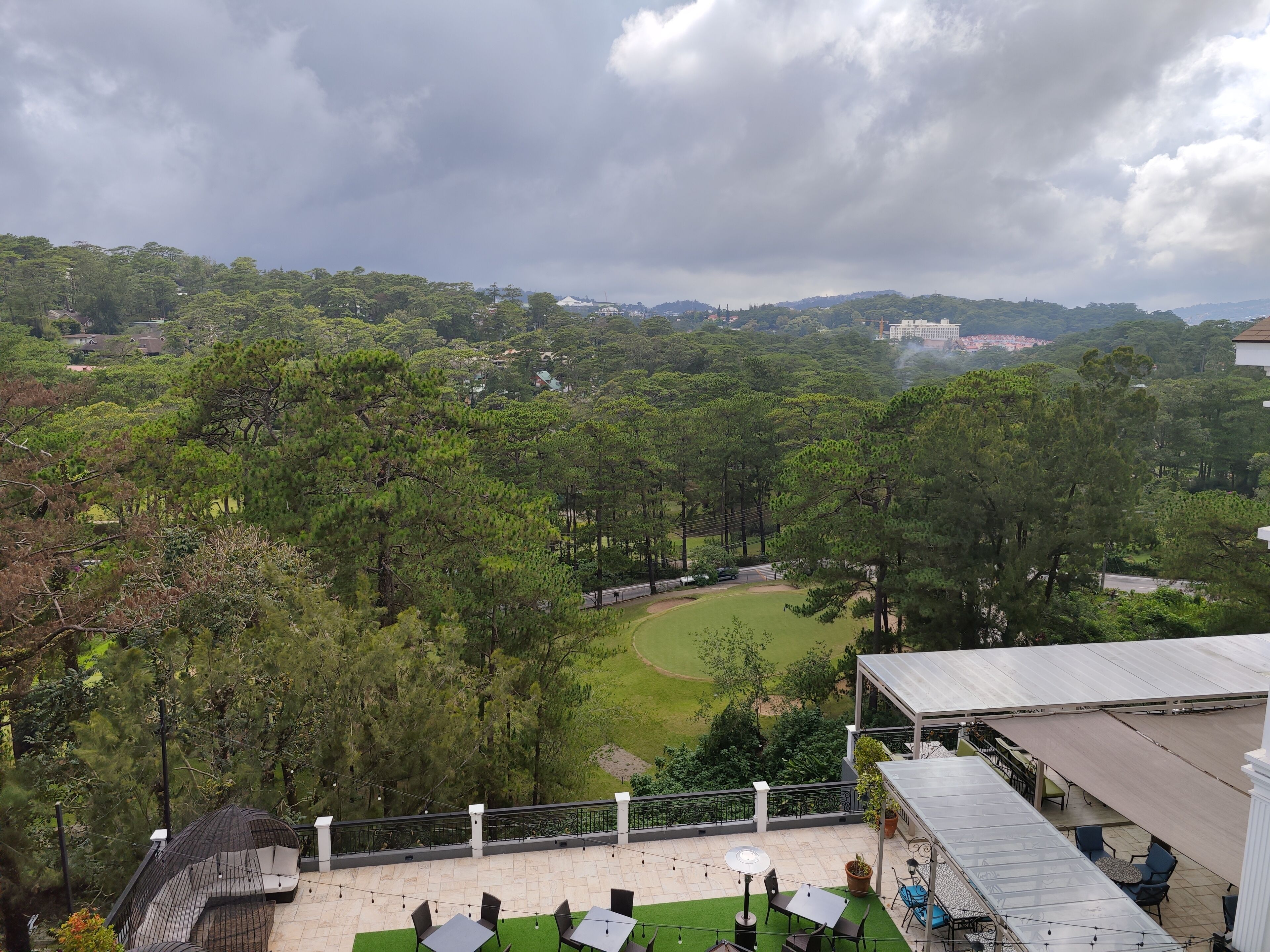 A rooftop terrace with outdoor seating, a view of a golf course, and surrounding greenery.