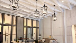 Un vestíbulo amplio con techo alto, ventanas grandes y muebles modernos, incluyendo sofás y mesas.