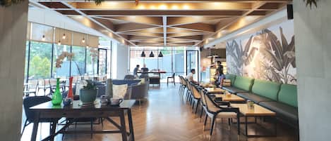 A spacious indoor area with wooden flooring, multiple seating arrangements including tables and chairs, and a large mural on the wall.