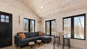 Et moderne interiør i en træhytte med en hjørnesofa, et spisebord med barstole og store vinduer med udsigt over den omkringliggende skov.