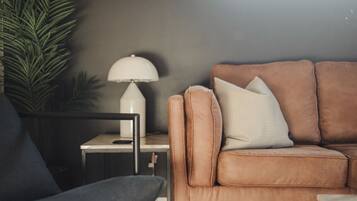 A living room with a brown sofa, a small side table, a lamp, and a potted plant.