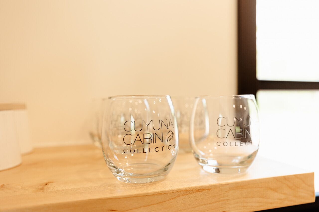 Two clear glass cups with the text "CUYUNA CABIN COLLECTION" on a wooden surface.