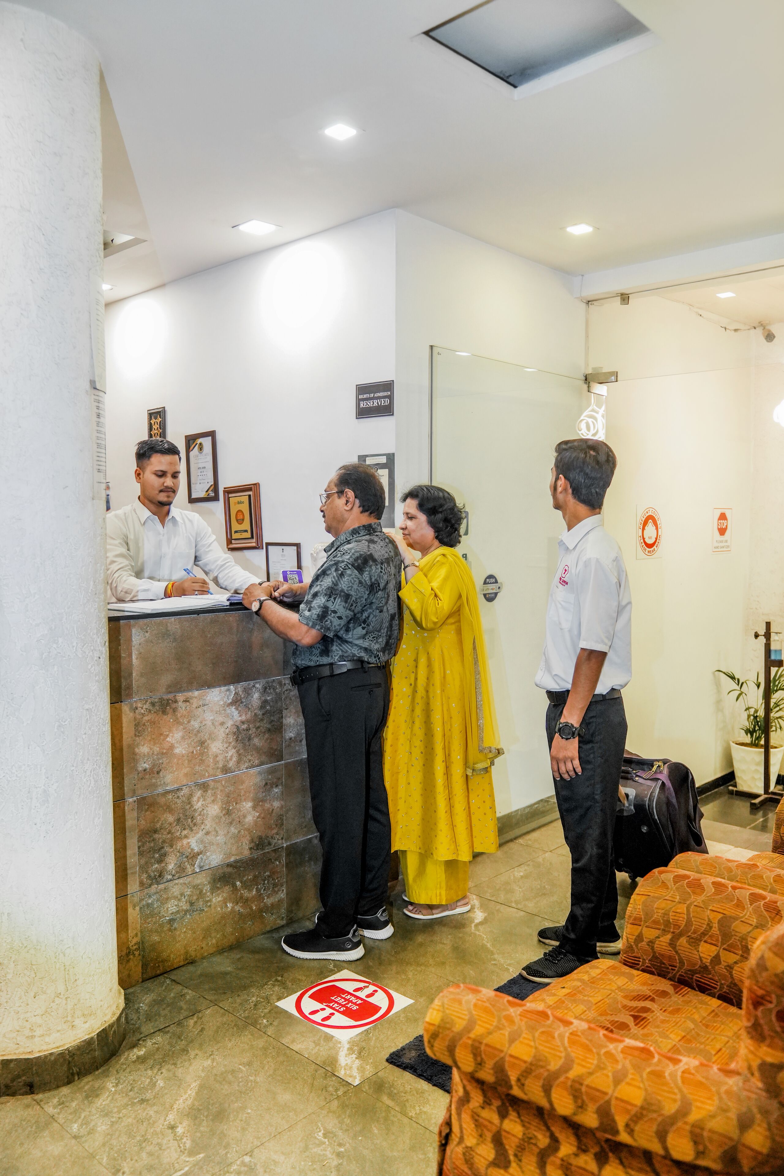 Zona de recepción con mostrador, puerta de vidrio y área de descanso con cojines estampados.