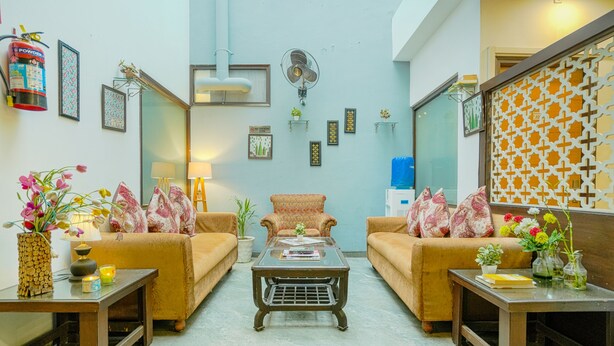 A living room with two sofas, a coffee table, and a fan on the wall. - Hotel Seven - Centre of City Chandigarh (Chandigarh)