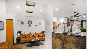 A reception area with a receptionist, a sofa with patterned cushions, a clock, and a large pillar. - Hotel Seven - Centre of City Chandigarh (Chandigarh)