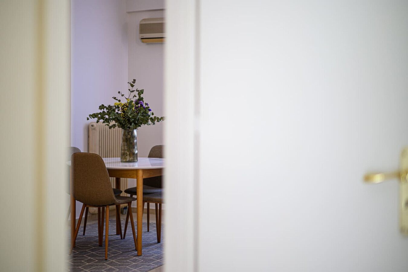 A dining area with a round table, chairs, and a vase with flowers.