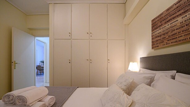 A hotel room with a bed, pillows, a folded towel, a wardrobe, and a wall with text. - Anna’s apartment Historic Center (Kalamata)