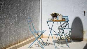 A blue metal chair and table set against a textured wall, with a small potted plant and a few items on the table. - Anna’s apartment Historic Center (Kalamata)