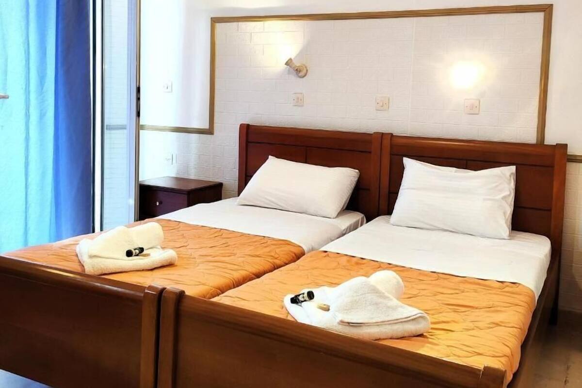 A double bed with white linens and a wooden headboard, two pillows, and a small bedside table with a lamp.