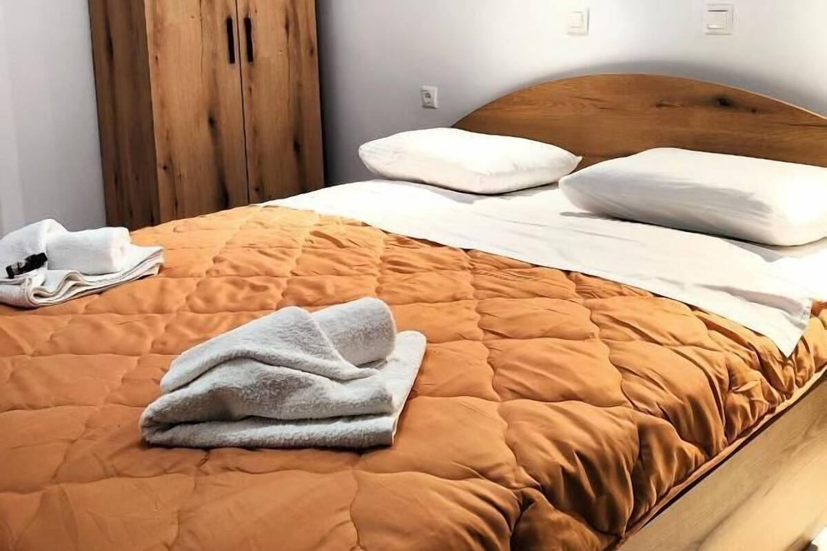A neatly made bed with a brown quilt, two white pillows, and a folded towel on the left side.