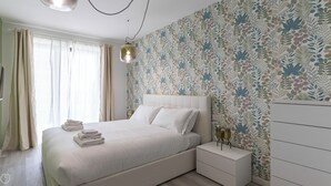 Une chambre à coucher moderne avec un grand lit, une table de chevet, une commode et un papier peint à motifs.