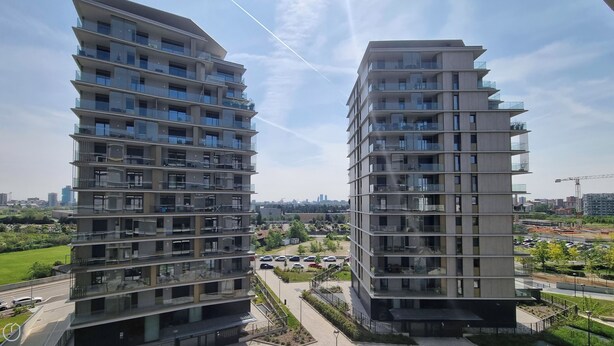 Deux immeubles résidentiels de grande hauteur, dotés de balcons, un espace de stationnement et une grue de construction en arrière-plan.