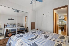 Une chambre avec un grand lit, un ventilateur de plafond, une porte en bois et une vue sur un balcon.