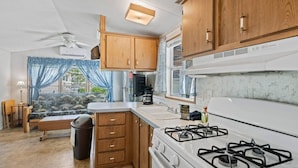A compact kitchen with wooden cabinets, a gas stove, and a small dining area with a sofa and table. - Magical Location on the River, Hiking, and Rafting (Sylva)