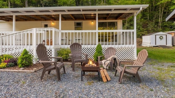 A covered outdoor seating area with Adirondack chairs and a fire pit. - Magical Location on the River, Hiking, and Rafting (Sylva)